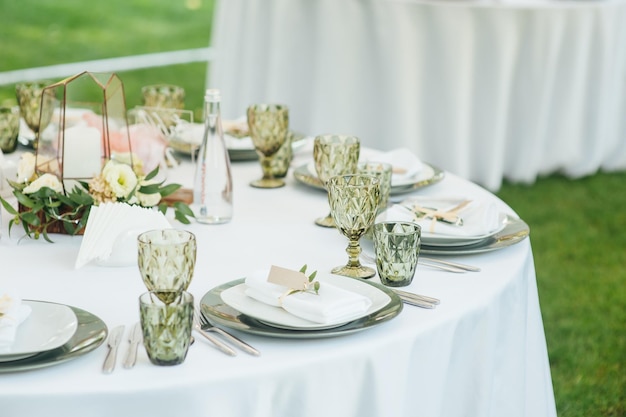 Bruiloftsbanket De stoelen en ronde tafel voor gasten geserveerd met bestek groen bloemen en servies en bedekt met een wit tafelkleed olijfkleur