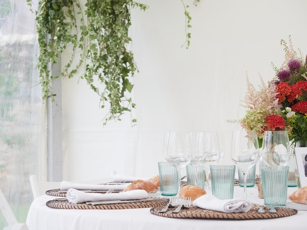 Bruiloftsdecoratie Natuurstijl met groene bladeren planten Tafelopstelling met bloemen Wit tafelkleed en witte achtergrond met kopieerruimte