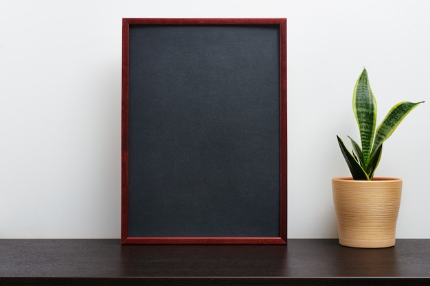 Bruin houten frame of schoolbordmodel in staande oriëntatie met een cactus in een pot op donkere werkruimtetafel en witte achtergrond