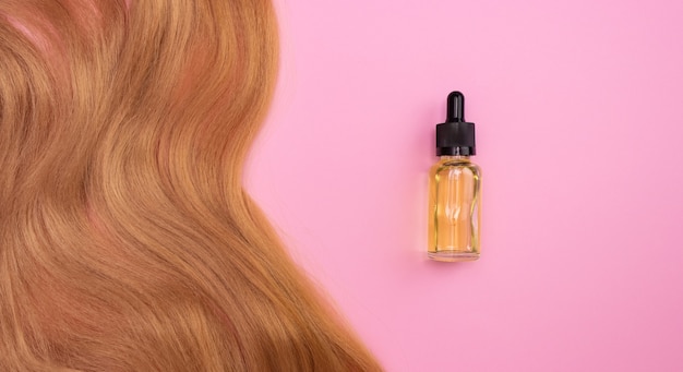 Bruin kunsthaar op roze en cosmetische olie in een glazen flesje met een pipet