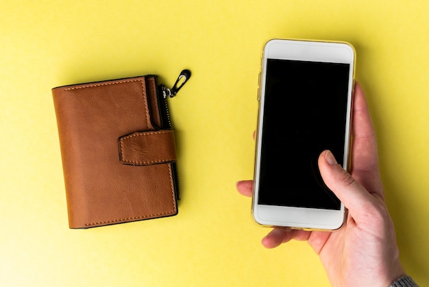 Bruin lederen portemonnee en mobiele telefoon op gele achtergrond.