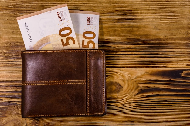 Foto bruin lederen portemonnee met vijftig eurobankbiljetten op de houten achtergrond. bovenaanzicht