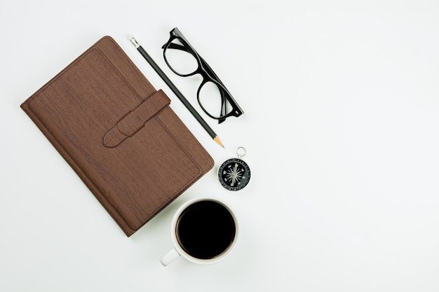 Bruin leernotitieboekje en een koffiekop op witte bureauachtergrond