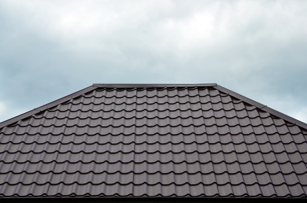 Bruine daktegels of dakspanen op huis als achtergrond. Nieuw overlappend bruin klassiek dakwerkmateriaaltextuurpatroon op een echt huis