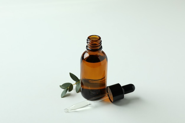 Bruine fles eucalyptusolie en takje op witte achtergrond