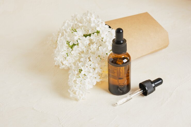 Bruine fles met een druppelaar voor cosmetische oliën of serums en een tak van witte lila op een beige achtergrond, natuurlijke cosmetica voor lichaams- en gezichtshuidverzorging.
