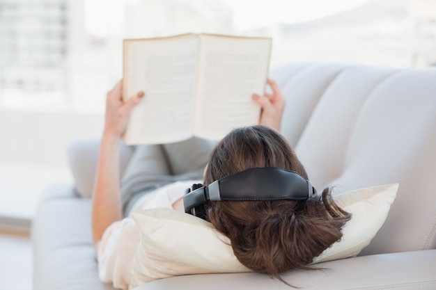 Bruine haired vrouw die van muziek geniet terwijl het lezen van een boek