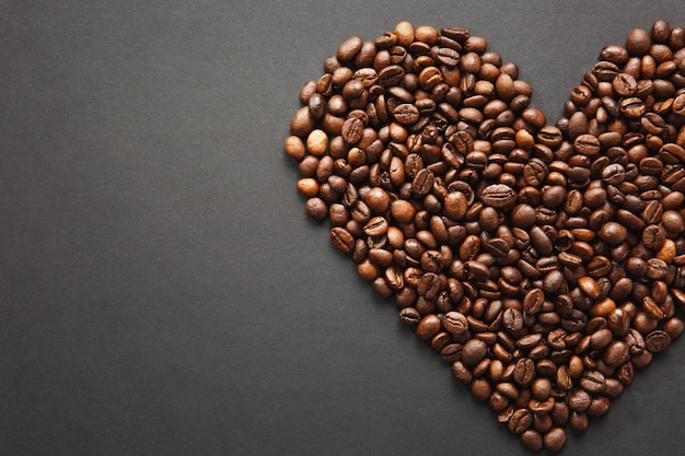Bruine koffiebonen in de vorm van een hart geïsoleerd op een zwarte textuurachtergrond voor ontwerp, een deel of de helft. Saint Valentine's Day-kaart op 14 februari, vakantieconcept.