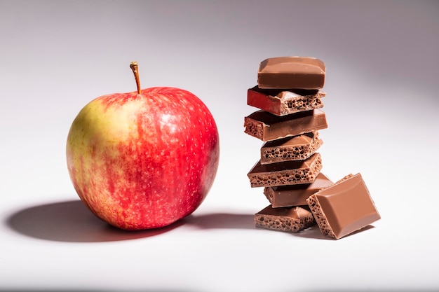 Bruine poreuze chocolade en een rode appel op een witte tafel.