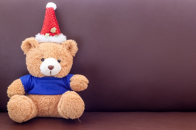 Bruine teddybeer met blauw overhemd die Kerstmishoed op de bank dragen