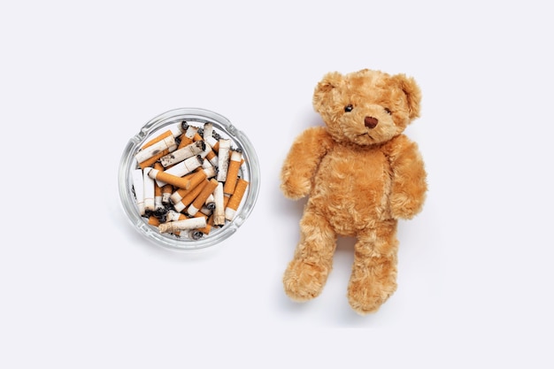 Bruine teddybeer met sigarettenpeuken en as op witte achtergrond.