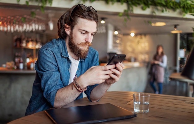 Bruinharige jongeman met baard en stuursnor met smartphone in een loftcafé