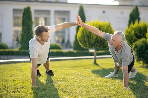 Bruinharige man en grijsharige man staan in plank pose, high five geven