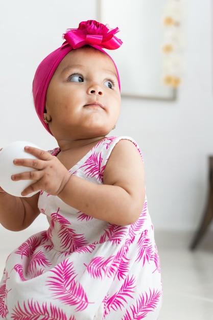 Bruinhuidig babymeisje dat op de vloer zit te spelen met een wit ballenmeisje dat achteruit kijkt