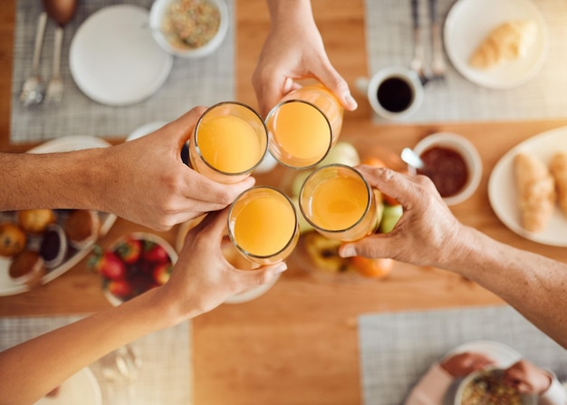 Le mani del brunch o le persone brindano con succo d'arancia, bevanda o bevanda in vetro a pranzo, colazione o pasto, frutta, liquido, vista dall'alto, gruppo o amici di casa, festeggiano il sostegno o brindano all'evento di riunione