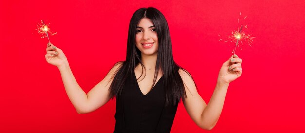 A brunette in a black dress on a red background holds sparklers Festive mood Panoramic photo