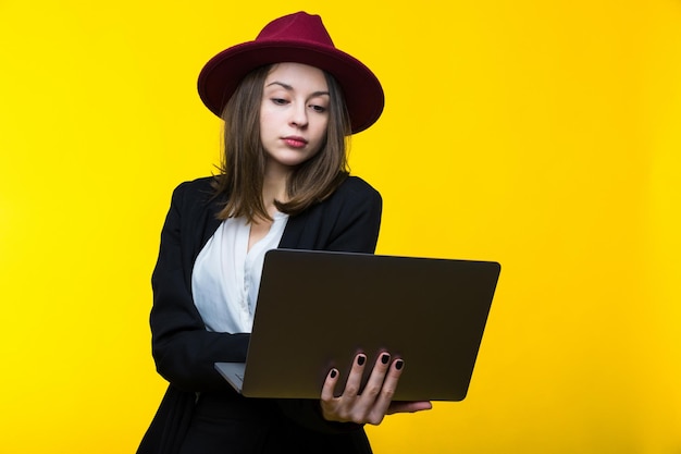 A brunette in a black suit and hat is working with a laptopBusiness photography in the studio