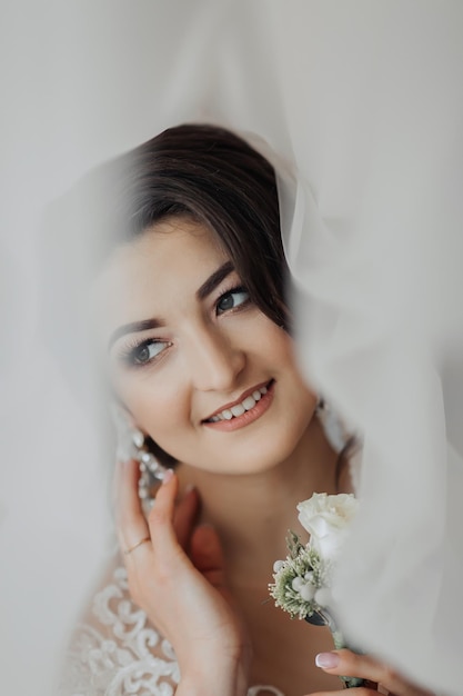 A brunette bride in a white dress holds her wedding bouquet poses French manicure Open shoulders Beautiful hands Long veil Morning of the bride Details