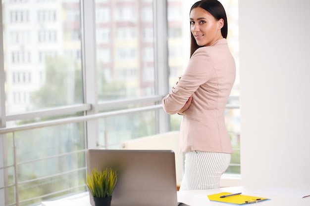 Brunette business lady in suit standing in bright office arms crossed smiling