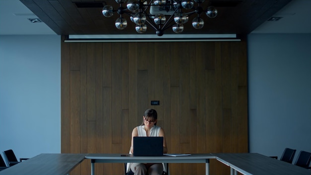 Brunette businesswoman working laptop computer in empty conference room alone