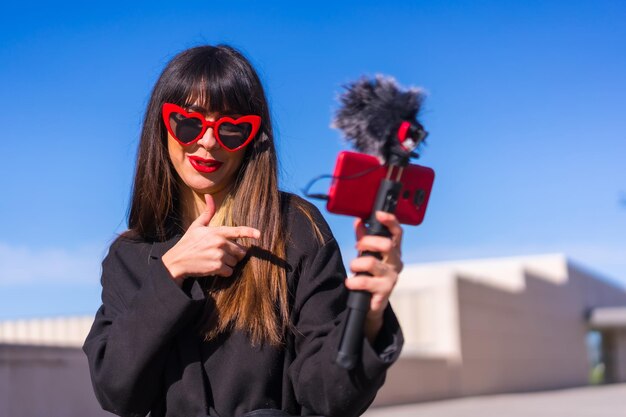 Brunette caucasian girl making a vlog on Valentines day for social networks red hearts sunglasses talking on the phone and microphone