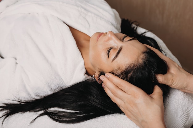 Donna caucasica castana che ha massaggio alla testa al salone durante una procedura della stazione termale