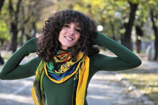 Foto bruna giovane donna carina con sciarpa colorata sorridente all'aperto in natura