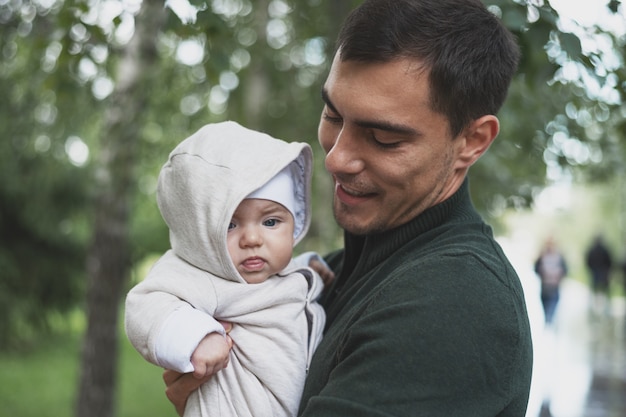 Brunette dad in green jacket with baby in his arms in Park, daddy's care concept