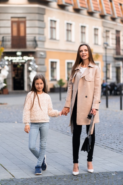 Brunette dame wandelen met haar mooie dochter op straat achtergrond in herfstdag.