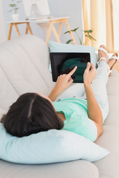 Brunette die haar tablet op bank gebruiken