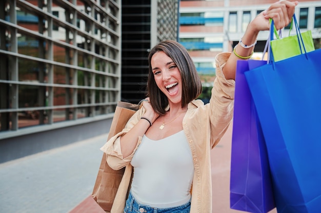 Foto brunette echte jonge vrouw met winkelzakken die haar gekochte nieuwe outfit laat zien glimlachend met een