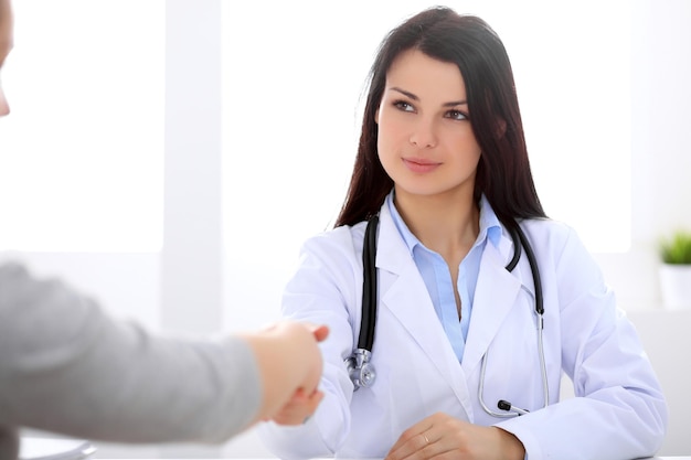 Brunette female doctor shaking hands with patient during a conversation with her.