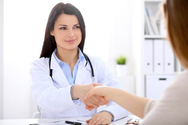 Brunette female doctor shaking hands with patient during a conversation with her.