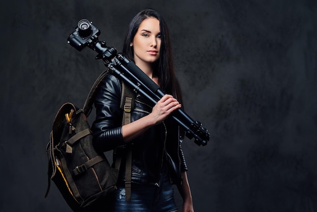 Brunette female photographer holds professional camera on a tripod and traveler backpack.