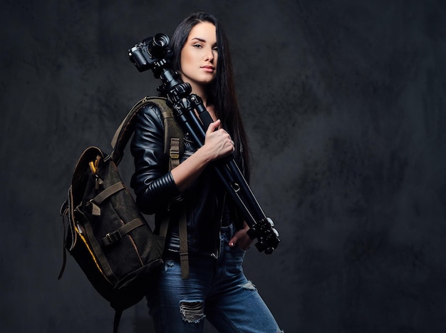 Brunette female photographer holds professional camera on a tripod and traveler backpack.