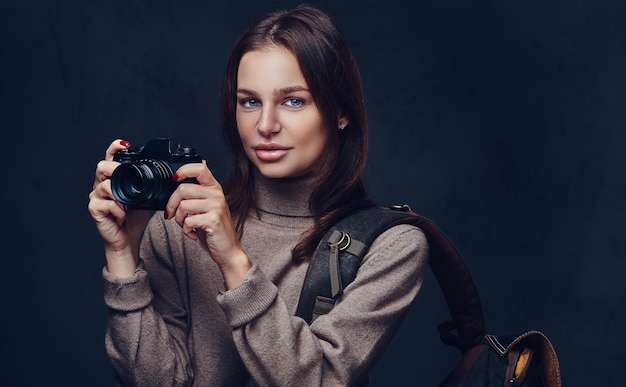 A brunette female traveler with backpack holds compact photo camera.