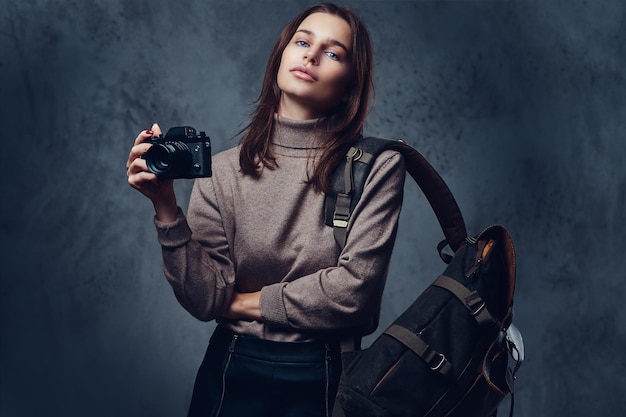 A brunette female traveler with backpack holds compact photo camera.