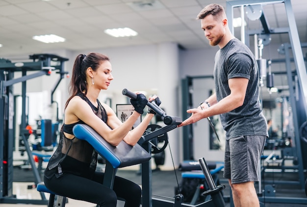 Brunette fitness meisje traint in een sportschool met een halterschijf. Trainer helpt om betere resultaten te behalen.