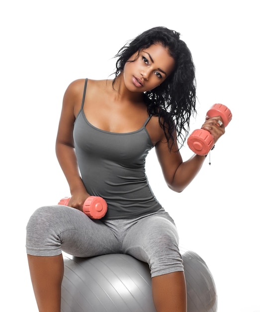 Brunette fitness woman in grey sportswear sitting on fitness ball and holding dumbell.