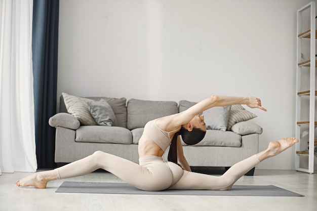 Brunette fitte vrouw in beige leggins en top die thuis yoga op mat doet