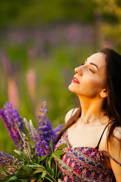 Brunette in a flower field.the girl holds lupines purple