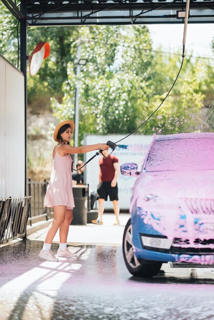 Brunette from a highpressure hose applies a cleaner on the car