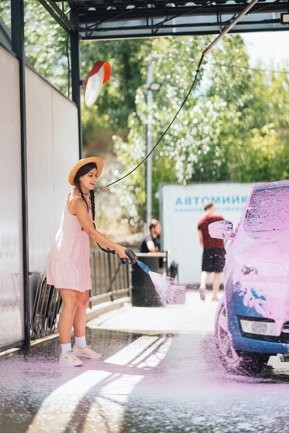 Brunette from a highpressure hose applies a cleaner on the car