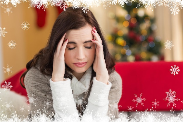 Brunette getting a headache on christmas day against fir tree forest and snowflakes