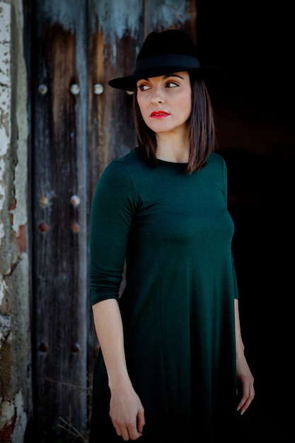 Brunette girl in black with a stylish hat and a old wooden door of background