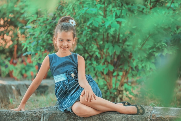 A brunette girl in a blue polka dot dress sitting in the park in the summer. High quality photo