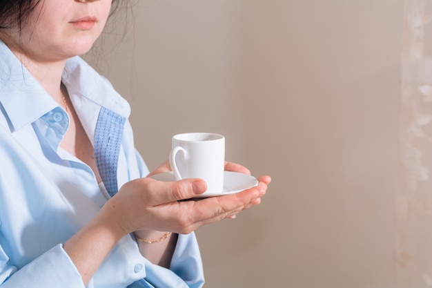 一杯のコーヒーを保持し、ベッドで楽しんでいる青いシャツのブルネットの少女