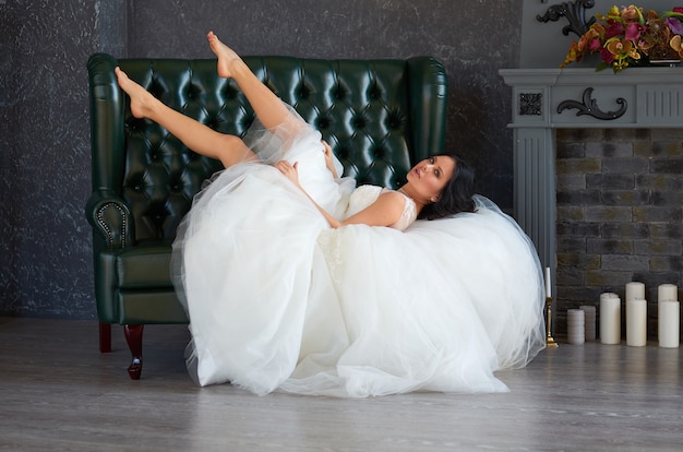 Brunette girl bride in a wedding dress on a green leather sofa