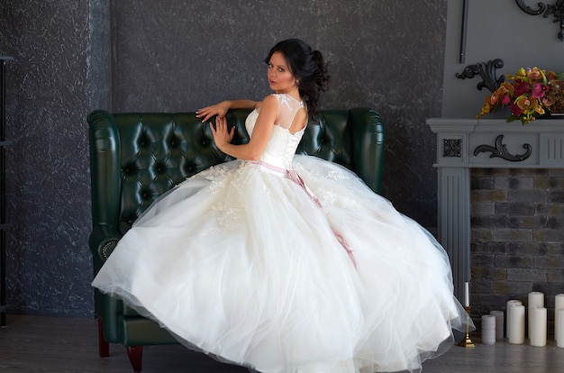 Brunette girl bride in a wedding dress on a green leather sofa