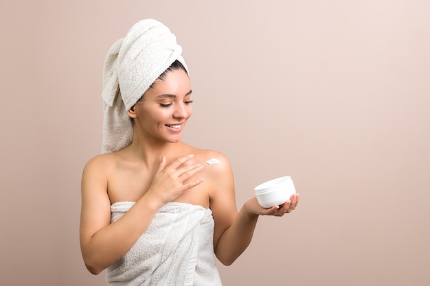 brunette girl dressed with a towel applying cream